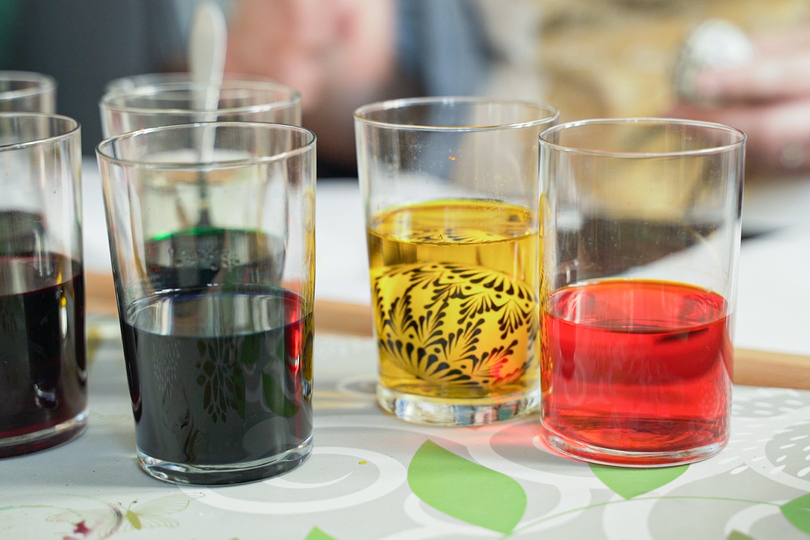 cztery szklanki wypełnione do połowy kolorowym płynem, dwie zielonym, jedna żółtym, a jedna czerwonym. W szklance z żółtym płynem zamoczone jajko