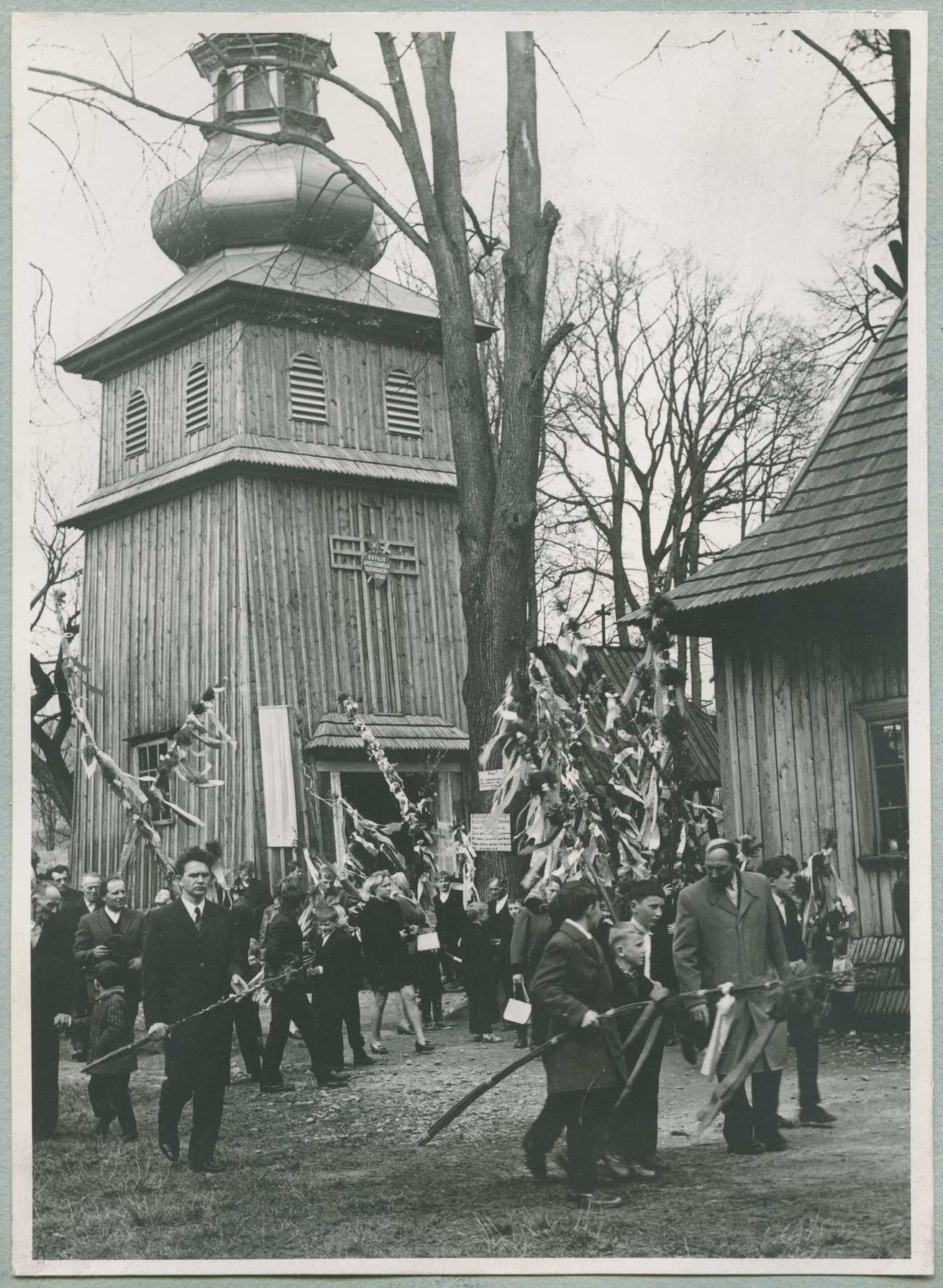 Duża grupa ludzi ubranych odświętnie przed kościołem z palmami